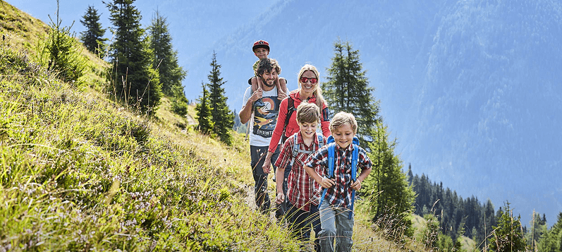 Une famille heureuse de cinq personnes avec des enfants marchant sur un sentier de montagne.