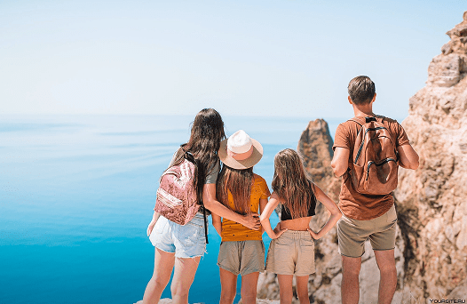 Une famille de quatre personnes debout sur une montagne, dos à nous, regardant au loin vers la mer.