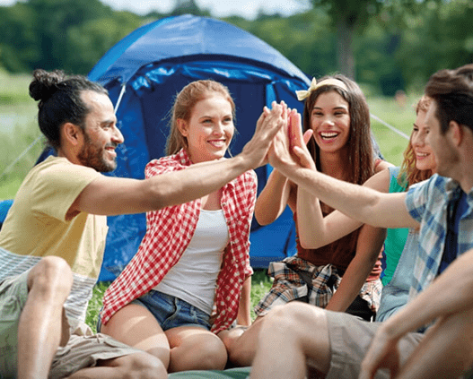 Cinq personnes heureuses assises en cercle devant une tente, se donnant un high-five.