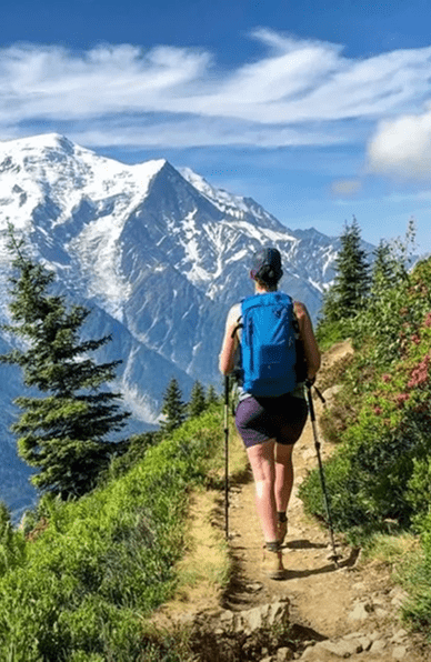 Un homme avec des bâtons de randonnée et un sac à dos marche sur un sentier de montagne avec une vue sur les sommets.