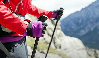 Une femme dans les montagnes, gros plan sur ses mains avec des bâtons de randonnée.